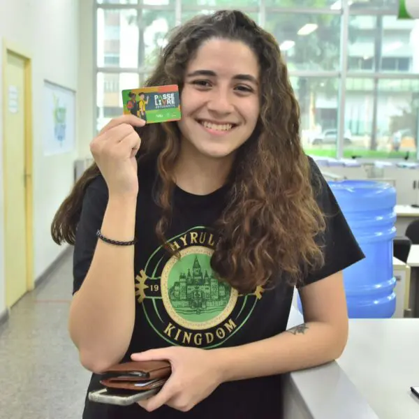 Uma garota branca vestindo camiseta preta e segurando o cartão do PLE