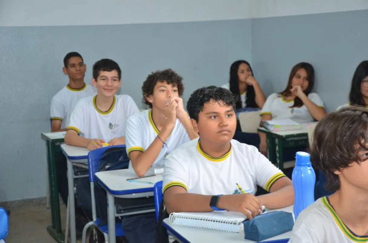 Estudantes sentados em carteiras enfileiradas, em sala de aula.