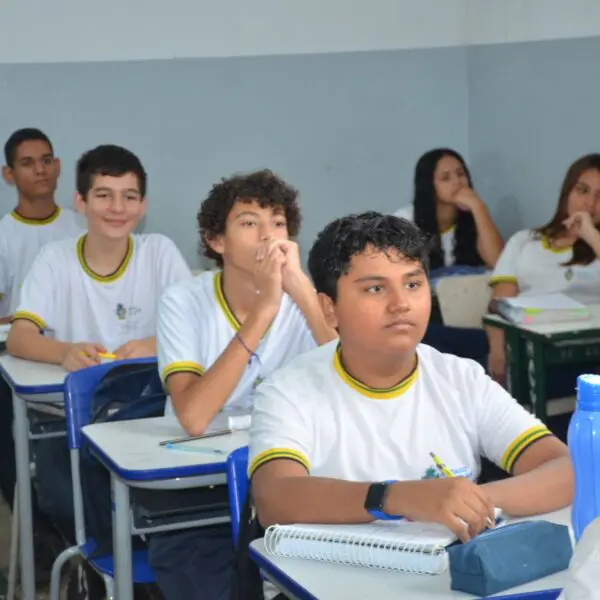 Estudantes sentados em carteiras enfileiradas, em sala de aula.