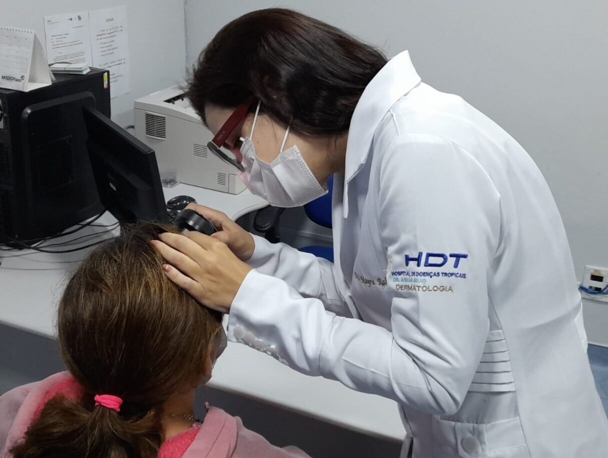 Médica do HDT examinando a pele de uma paciente com uma lupa.