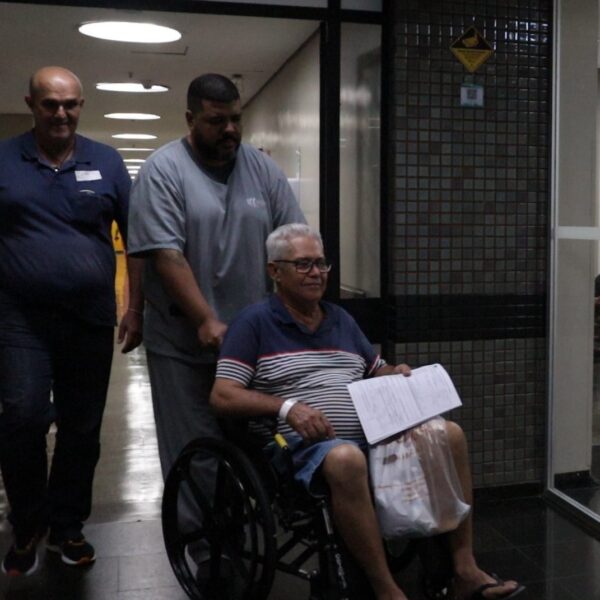 Paciente sendo transportado em cadeira de rodas no corredor do HGG
