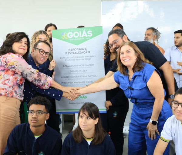 Colégios estaduais históricos da região de Campinas, em Goiânia, recebem investimentos - secretária e diretora em aperto de mãos à frente de placa de inaugurações. Ao lado delas, membros da comunidade escolar