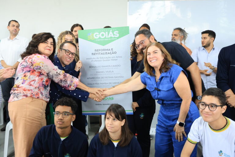 Colégios estaduais históricos da região de Campinas, em Goiânia, recebem investimentos - secretária e diretora em aperto de mãos à frente de placa de inaugurações. Ao lado delas, membros da comunidade escolar